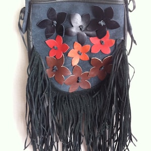 Könnte beinhalten: Eine kleine schwarze Wildledertasche mit Fransenbesatz. Die Tasche ist mit bunten Lederblumen in Rot-, Orange-, Braun- und Schwarztönen verziert.