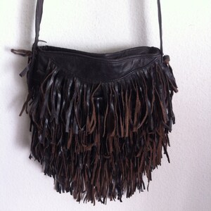 May include: A brown leather shoulder bag with a fringe detail. The fringe is made of both brown and black leather.