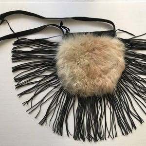 May include: A black leather crossbody bag with a fluffy, light brown fur pouch and long black fringe.