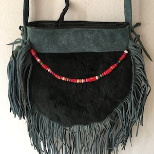 May include: A dark green suede and fur crossbody bag with a fringe trim and colorful beaded detail.