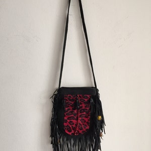 May include: A black leather crossbody bag with a red and black leopard print flap. The bag has fringe detailing and gold beads.