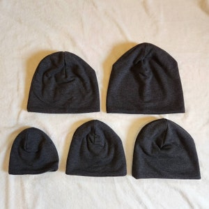 May include: Four gray knit beanies of varying sizes. The beanies are all made of a soft, stretchy fabric and have a simple, classic design.