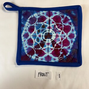 May include: Square, tie-dye pot holder with a blue border and hanging loop. The center features a circular design in shades of purple and blue, with white stitching. The word "Front" is written on a small white label.
