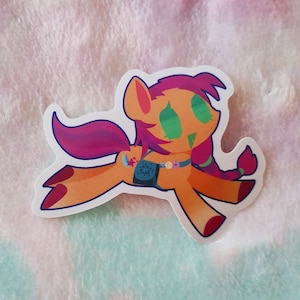 Könnte beinhalten: Ein Aufkleber mit einem Cartoon-Pony mit orangefarbenem Fell, rosa und violettem Haar und grünen Augen. Das Pony trägt einen blau-weißen Rucksack und eine Halskette mit bunten Perlen. Das Pony rennt und hat einen Stern auf seinem Bein.
