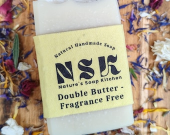 Könnte beinhalten: Ein rechteckiges Stück cremeweiße Seife, umwickelt mit einem gelben Papieretikett. Das Etikett trägt den schwarzen Text Natural Handmade Soap, NSK, Nature's Soap Kitchen, Double Butter und Fragrance Free. Die Seife hat eine glatte Textur.