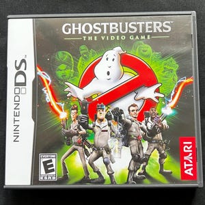 May include: A Nintendo DS game case for "Ghostbusters: The Video Game." The cover features the Ghostbusters team, the iconic no-ghost logo, and green spectral figures. The Atari logo is visible.