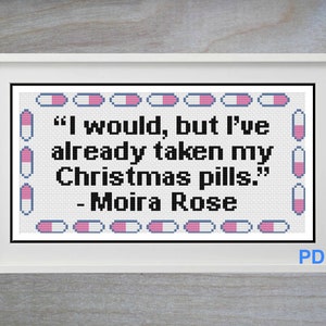 May include: A white framed cross-stitch pattern featuring a quote from the TV show Schitt's Creek. The quote reads "I would, but I've already taken my Christmas pills." - Moira Rose. The pattern is surrounded by a border of pink and blue pills.