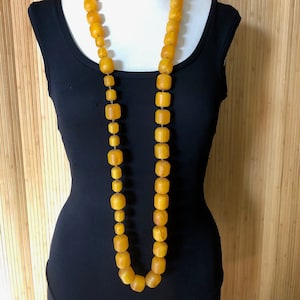 May include: A long necklace made of large, chunky, amber-colored beads. The beads are all roughly the same size and shape, and they are strung together on a thin, gold-colored chain.