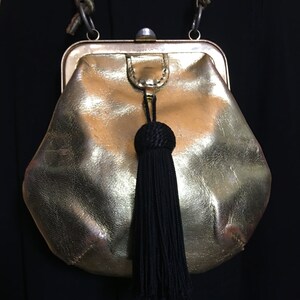 May include: A gold-colored leather purse with a black tassel. The purse has a clasp closure and a chain strap.