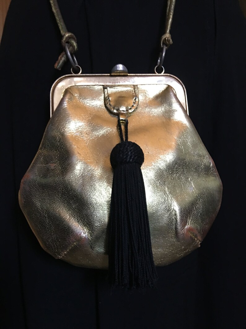 May include: A gold-colored leather purse with a black tassel. The purse has a clasp closure and a chain strap.