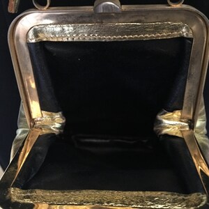 May include: A gold-toned metal purse with a black fabric lining. The purse is open and the inside is visible.
