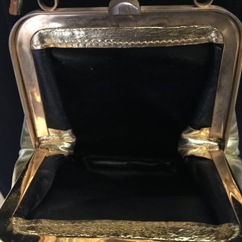 May include: A gold-toned metal purse with a black fabric lining. The purse is open and the inside is visible.