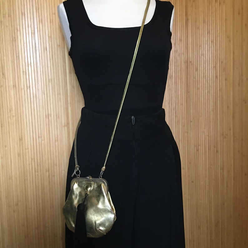 May include: A gold-colored chain strap purse with a clasp closure. The purse is worn over a black sleeveless top and black skirt.