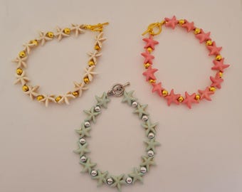 Puede incluir: Tres pulseras con cuentas en forma de estrella. Una pulsera es de color blanco roto con cuentas doradas, otra es rosa con cuentas doradas y la tercera es verde claro con cuentas plateadas. Cada pulsera tiene un cierre diferente.