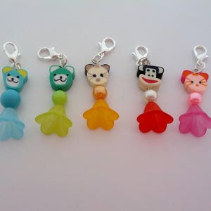 Op de afbeelding: Vijf kleurrijke bedelhangers met zilverkleurige sluitingen. Elke bedel heeft een cartoon dierengezicht, kralen en een bloemvormig accent. De bedels zijn in tinten blauw, groen, oranje, rood en roze.