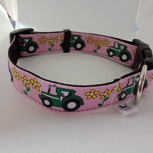 Op de afbeelding: Roze hondenhalsband met een herhalend patroon van groene tractoren en gele bloemen. De halsband heeft een zwarte gesp en een zilveren metalen ring voor het bevestigen van de lijn. Gemaakt van duurzaam materiaal.