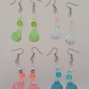 May include: Six pairs of dangle earrings with iridescent seashell charms. Each earring has a silver-tone hook, a chain of beads in various colours, and a shell-shaped charm. The colour combinations include green, pink, orange, and blue.