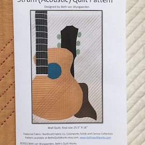 May include: A quilt pattern for a wall quilt featuring an acoustic guitar. The pattern is called "Strum (Acoustic)" and is designed by Beth van Wyngaarden. The quilt is 25.5 inches by 16 inches. The pattern is available at BethsQuiltWorks.etsy.com and www.bethsquiltworks.com. ©2021 Beth van Wyngaarden, Beth's Quilt Works.