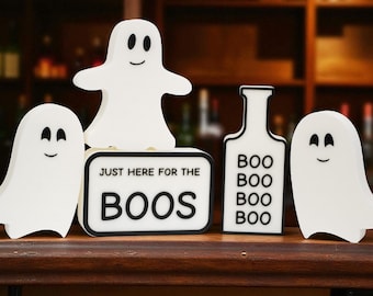 Può includere: Una collezione di decorazioni bianche a tema Halloween. Il set include quattro figure di fantasmi e un cartello con la scritta "JUST HERE FOR THE BOOS". Una decorazione a forma di bottiglia che ripete la parola "BOO".