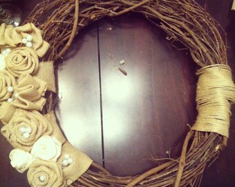 May include: A brown twig wreath decorated with burlap and white fabric flowers. The flowers have pearl accents.