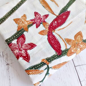 May include: White fabric with a repeating pattern of red, orange, and green flowers and leaves. The fabric has a subtle dotted pattern.