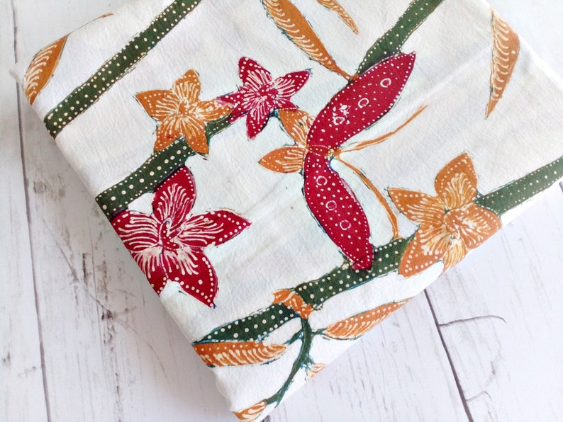 May include: White fabric with a repeating pattern of red, orange, and green flowers and leaves. The fabric has a subtle dotted pattern.
