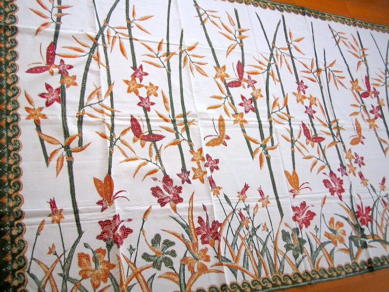 May include: White fabric with a repeating pattern of brown bamboo stalks, orange and red flowers, and butterflies. The fabric has a green border with a wave pattern.