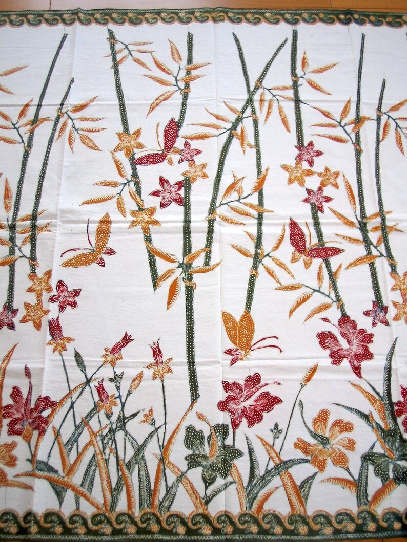 May include: White fabric with a repeating pattern of brown bamboo stalks, orange and yellow flowers, and red butterflies. The fabric has a green border with a wavy design.