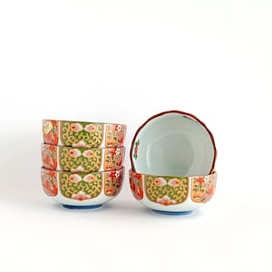 May include: Set of four small, white ceramic bowls with a colourful floral pattern in shades of red, orange, green, and blue. The bowls are stacked on top of each other.