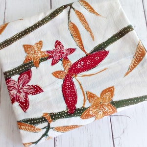 May include: White fabric with a floral pattern. The flowers are red, orange, and green. The fabric has a subtle texture.