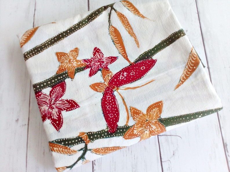May include: White fabric with a floral pattern. The flowers are red, orange, and green. The fabric has a subtle texture.