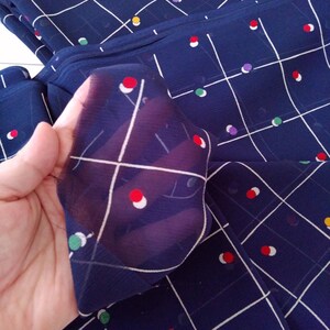 May include: Navy blue fabric with a white grid pattern and colorful circles. The fabric is sheer and has a soft, flowing texture.