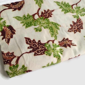May include: White fabric with a brown and green floral pattern. The fabric has a batik design with intricate details.