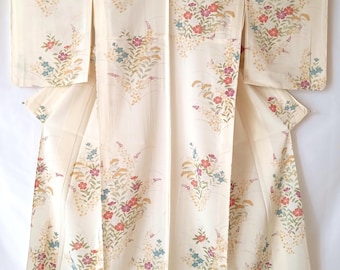 May include: A cream-colored kimono featuring a repeating pattern of floral clusters in shades of red, blue, and gold. The garment has wide sleeves, a central vertical seam, and a structured collar, displaying a symmetrical arrangement of botanical motifs.