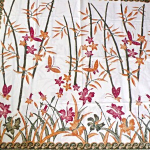 May include: White fabric with a repeating pattern of brown bamboo stalks, orange flowers, and pink butterflies. The fabric has a green border with a wave pattern.