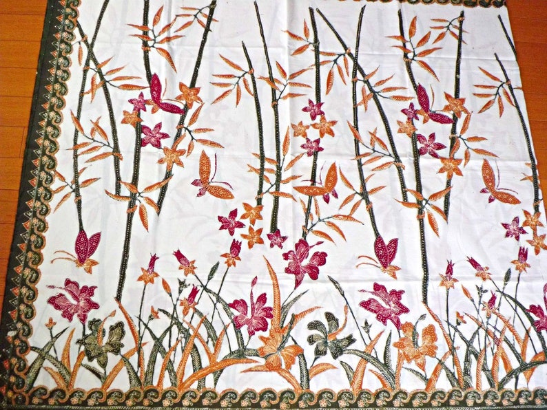 May include: White fabric with a repeating pattern of brown bamboo stalks, orange flowers, and pink butterflies. The fabric has a green border with a wave pattern.