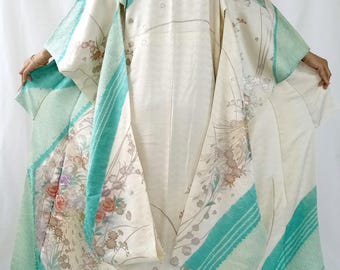 May include: A cream-colored kimono featuring wide sleeves and a flowing silhouette. The garment is decorated with vibrant teal geometric panels and delicate floral patterns in shades of pink, orange, and green, with a subtle wave-like texture.