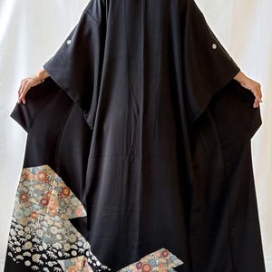 May include: A black kimono with a floral pattern in shades of orange, pink, and white. The kimono has wide sleeves and is made of a smooth, flowing fabric. The floral design is concentrated at the bottom.