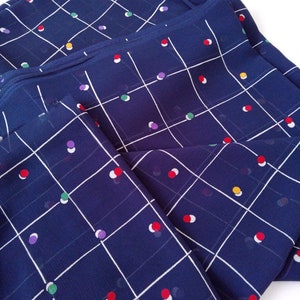 May include: A blue fabric with a white grid pattern and colorful polka dots. The fabric is folded in half and the polka dots are visible on both sides.