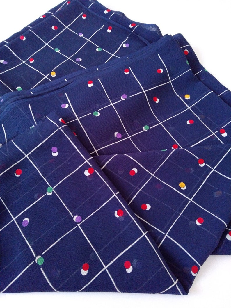 May include: A blue fabric with a white grid pattern and colorful polka dots. The fabric is folded in half and the polka dots are visible on both sides.