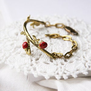Peut inclure: Un bracelet en or avec un motif de branche délicat et des accents de coccinelle rouge. Le bracelet est composé d'une chaîne et d'une branche incurvée avec des feuilles et des coccinelles.