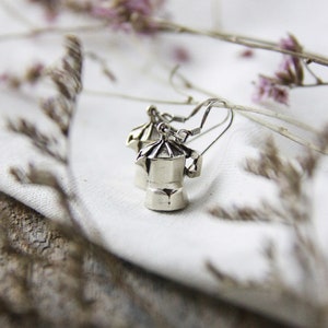 Puede incluir: Un par de pendientes de plata con forma de cafeteras en miniatura. Los pendientes son delicados y tienen un aspecto vintage.