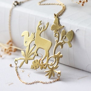 Puede incluir: Un collar de oro con una cadena delicada y un colgante con un ciervo, una ardilla, una mariposa y un pájaro recortados. El colgante está intrincadamente diseñado con detalles florales.