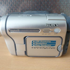 Peut inclure: Caméscope Sony Digital 8 argenté avec objectif noir et détails gris. Fonctions : USB Streaming, SteadyShot et Easy Handycam. Le caméscope porte le logo Sony sur son corps argenté.