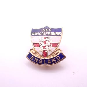 以下が含まれることがあります： イングランド1966年ワールドカップ優勝記念のヴィンテージピン。ピンは「1966 WORLD CUP WINNERS」と「ENGLAND」の文字が入った盾のデザインです。盾は白、赤、青で、金の縁取りが施されています。