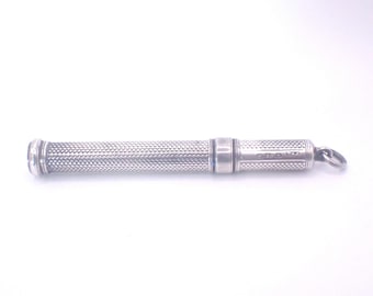 May include: A silver pencil holder with a textured, patterned design. The pencil holder is cylindrical with a rounded end and a small loop for attachment. The surface has a detailed, repeating pattern.