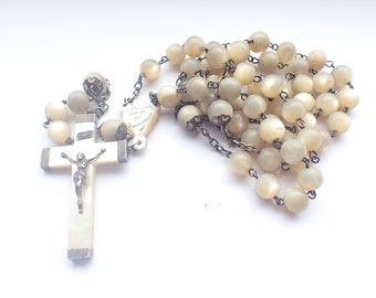 May include: Ivory-colored rosary with a crucifix and a series of round beads. The crucifix features a silver-toned figure of Jesus. The beads are connected by a silver-toned chain. The rosary is set against a white background.