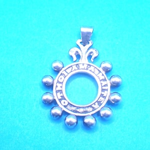 Peut inclure: Pendentif argenté de forme circulaire, avec un trou central et du texte. Le pendentif est orné de petits accents sphériques sur le bord extérieur. La bélière est de forme rectangulaire simple. Le pendentif est présenté sur fond bleu.