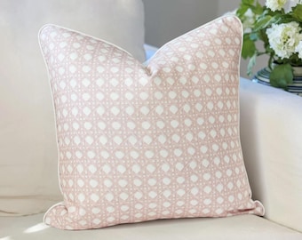 May include: A square throw pillow featuring a light pink and white cane webbing pattern. The pillow is finished with white piping along all four edges, creating a defined border. The fabric displays a repeating geometric octagonal weave design.
