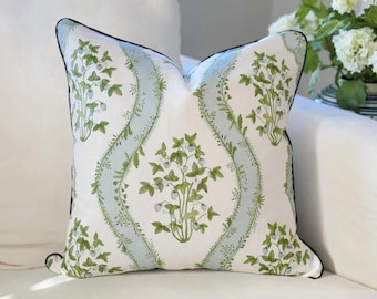 May include: A square throw pillow featuring a white background with a repeating pattern of green strawberry plants and light blue vertical wavy bands. The pillow is finished with a thin, dark navy blue piping along all four edges.